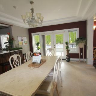 A well-lit dining room with a large table and elegant chairs, complemented by a chandelier and indoor plants.