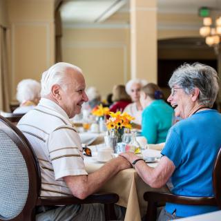 A group of seniors enjoying a meal and conversation in a communal dining area.