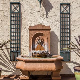 A decorative outdoor wall fountain in a garden setting.