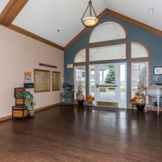 A spacious lobby with a high ceiling and large windows, featuring wooden floors and decorative elements.