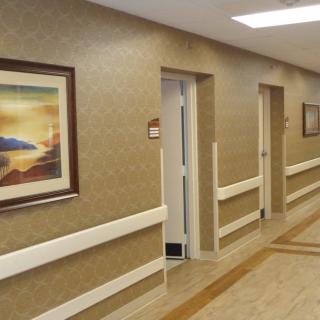 A hospital corridor with a painting on the wall and several doors.