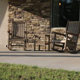 Two wooden rocking chairs on a sunny porch against a brick wall.