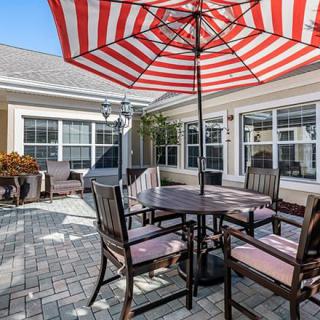 Outdoor patio with a red and white striped umbrella, surrounded by wooden chairs and a table.