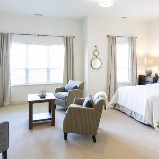 A modern, bright bedroom with large windows, featuring a bed and comfortable armchairs.
