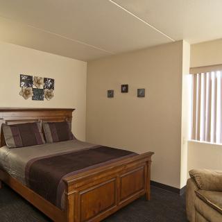 A cozy bedroom featuring a wooden bed with brown bedding, wall decor, and a window with blinds.