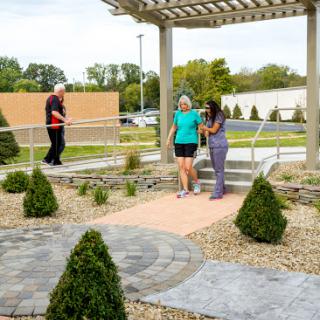Two individuals stroll through a landscaped garden while another person walks in the background.