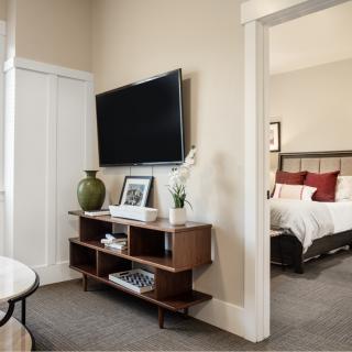A modern interior featuring a living area with a TV, shelves, and decor leading into a cozy bedroom.