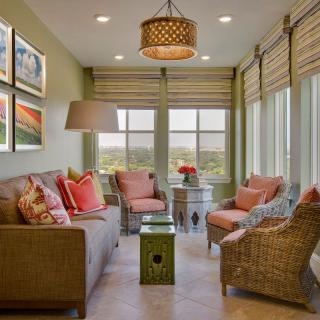 A cozy living room featuring a sofa, wicker chairs, and decorative pillows, with large windows letting in natural light.