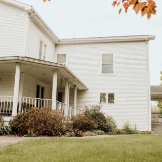 A suburban white house with a porch and a well-kept front yard, framed by autumn leaves.