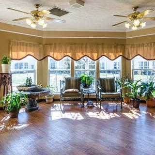 A bright living room with large windows, ceiling fans, and various potted plants.