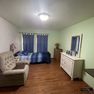 A cozy bedroom with a bed, dresser, and chair on hardwood flooring.
