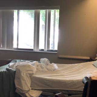 A hospital room with an unmade bed and natural light coming through the windows.