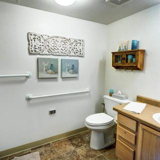 A well-organized bathroom featuring a toilet, sink, shelving with towels and toiletries, and decorative artwork on the walls.