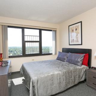 A cozy bedroom in an apartment with a neatly made bed and large window offering a view.