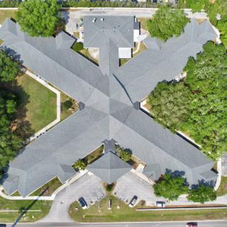 Aerial view of a large building with a distinctive X-shaped layout, surrounded by trees and a parking lot.