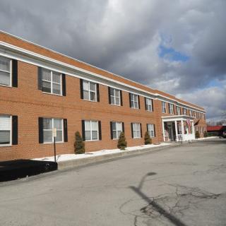 A brick building with multiple windows under a cloudy sky.