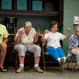 A group of elderly individuals participating in a seated exercise session indoors.