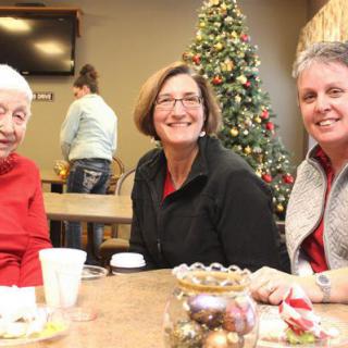A group of people sitting at a table with Christmas decorations in the background, enjoying a festive gathering.