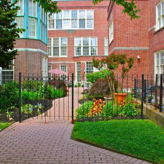 Charming garden nestled between red brick buildings with a gated pathway and lush greenery.