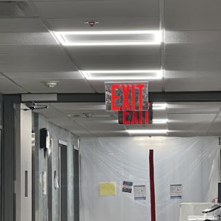 A view down a hallway featuring an illuminated exit sign and plastic barriers, indicating ongoing renovation work.