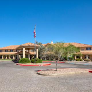 A wide-angle view of a large building with an American flag, surrounded by landscaping and a paved driveway under a clear blue sky.