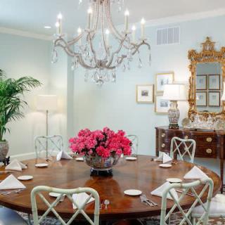 An elegantly decorated dining room featuring a chandelier, round table adorned with a floral centerpiece, and classic furnishings.