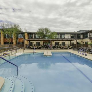 An outdoor swimming pool surrounded by loungers in a residential apartment complex under a cloudy sky.