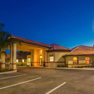 A warmly lit hotel exterior at night, showcasing a welcoming entrance and a spacious parking area.