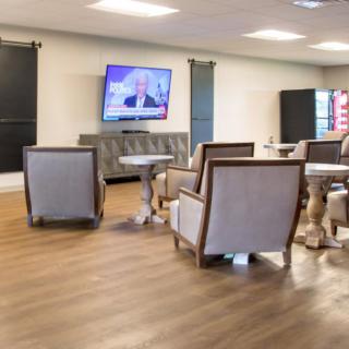 A modern lounge area with comfortable seating, a television, and several tables.