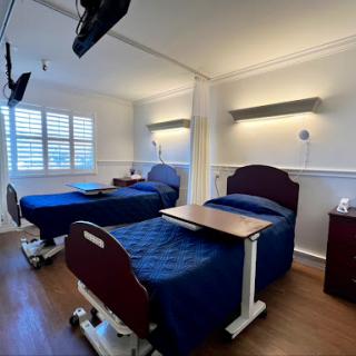 A well-lit hospital patient room with two adjustable beds and a warm, inviting atmosphere.