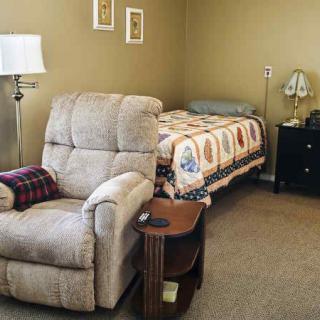 A cozy bedroom with a recliner chair, bed, lamp, and nightstand.