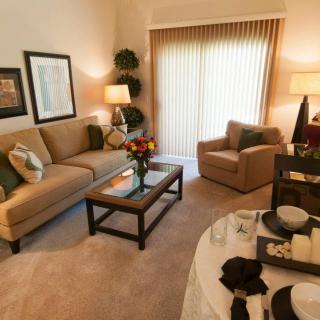 A cozy and well-decorated living room featuring a sofa, armchair, coffee table, and dining area with warm lighting.
