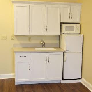 A compact kitchen setup featuring white cabinets, a small fridge, microwave, sink, and countertop.