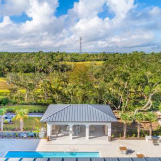 A poolside pavilion surrounded by lush greenery and a bright, cloudy sky.