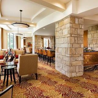 A modern hotel lounge featuring comfortable seating, stone walls, and a bar counter with ample natural lighting.