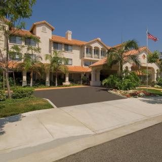 A large, multi-story building surrounded by palm trees and a driveway, with an American flag flying in front.