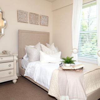 A cozy and modern bedroom featuring white bedding and minimalist decor, bathed in natural light from a nearby window.