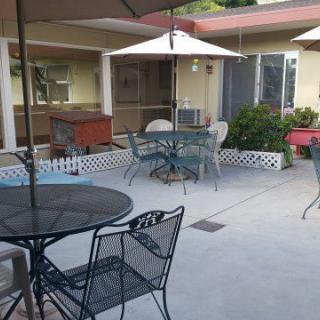 An outdoor patio area with metal tables and chairs, shaded by umbrellas.
