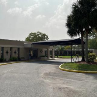 A building entrance with a covered driveway surrounded by palm trees under a cloudy sky.
