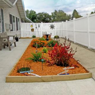 A well-maintained garden with colorful flowers and mulch next to a patio, enclosed by a white fence.