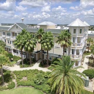 A multi-story residential building surrounded by lush greenery and palm trees under a partly cloudy sky.