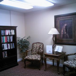 A cozy waiting room with a bookshelf, chairs, and a lamp.