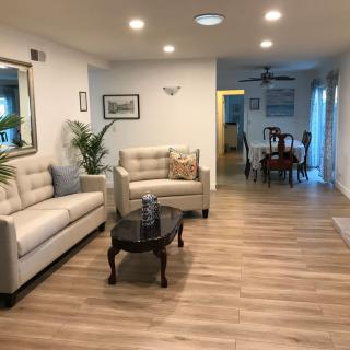A cozy living room with modern decor and hardwood flooring, featuring comfortable sofas and a coffee table, leading to a dining area.