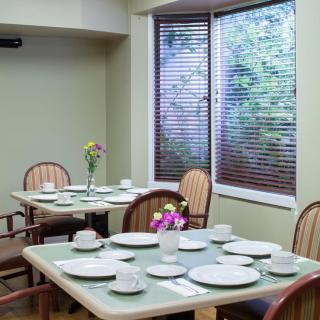 A neatly set dining room with tables and chairs, featuring plates and flowers by the window.