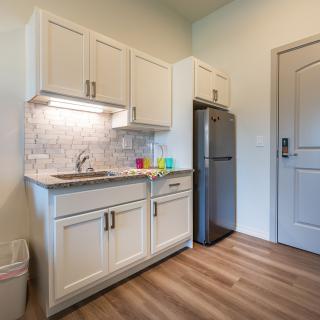 A modern kitchen area with white cabinets, a stainless steel sink, and a refrigerator.