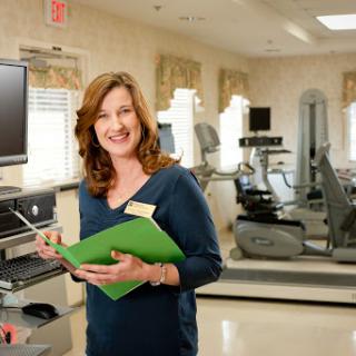 A welcoming professional in a fitness and rehabilitation center, holding documents and ready to assist.