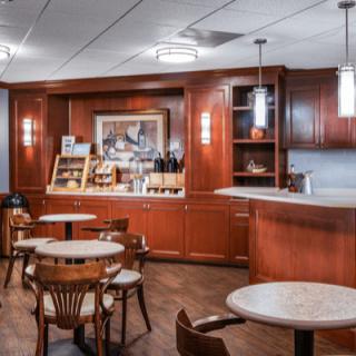 A cozy cafe interior with wooden tables and chairs, featuring a counter area and artwork on the wall.