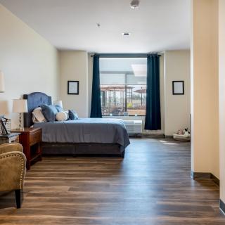 A spacious bedroom with a large bed and armchair, featuring hardwood floors and a window with curtains.