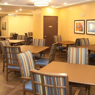 An empty dining area with striped chairs and wooden tables, featuring warm lighting and framed artwork on the walls.