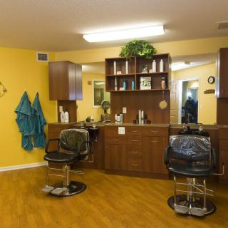 Interior of a barber shop with two chairs, mirrors, and shelves against yellow walls.